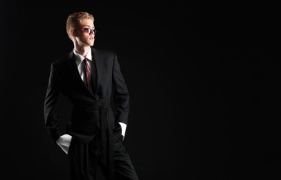 Photo of Handsome young man wearing stylish suit and sunglasses on black background, space for text