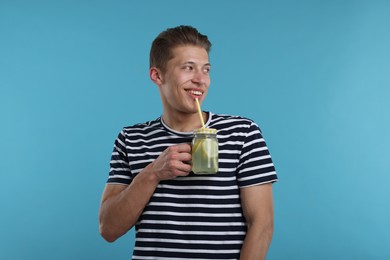 Photo of Smiling man drinking lemonade from mason jar on light blue background. Refreshing drink