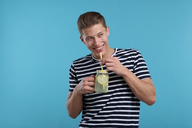 Photo of Smiling man drinking lemonade from mason jar on light blue background. Refreshing drink