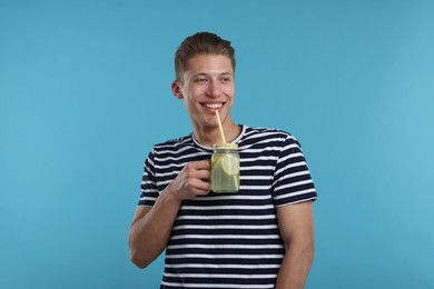 Photo of Smiling man drinking lemonade from mason jar on light blue background. Refreshing drink