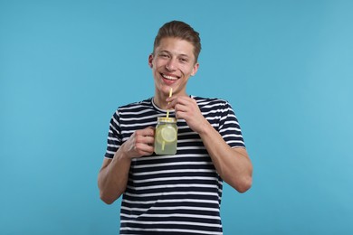 Photo of Smiling man drinking lemonade from mason jar on light blue background. Refreshing drink