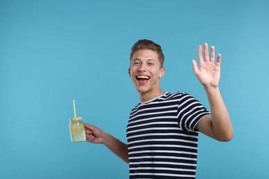 Photo of Happy man with mason jar of lemonade on light blue background. Refreshing drink