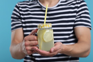 Photo of Man with mason jar of lemonade on light blue background, closeup. Refreshing drink