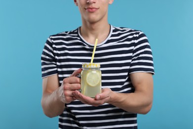 Photo of Man with mason jar of lemonade on light blue background, closeup. Refreshing drink
