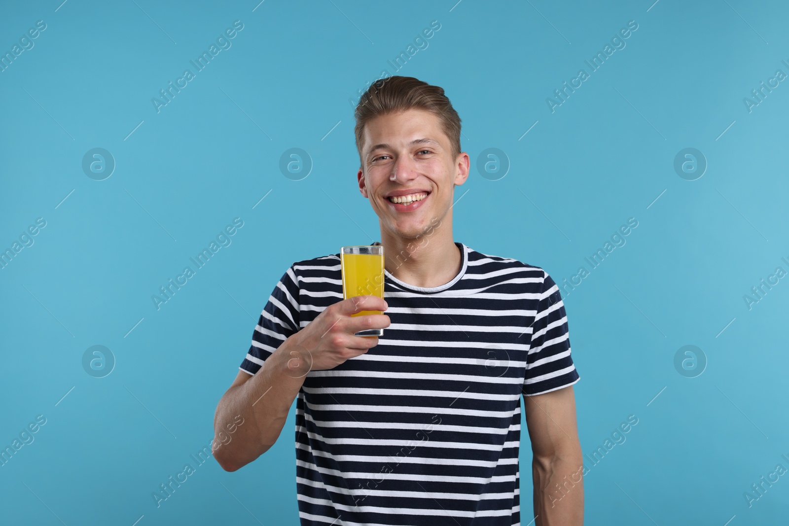 Happy man with glass of orange juice on light blue background. Refreshing drink Photo of Happy man with glass of orange juice on light blue background. Refreshing drink