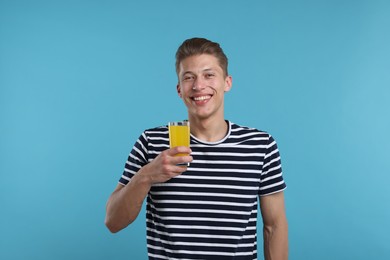 Photo of Happy man with glass of orange juice on light blue background. Refreshing drink