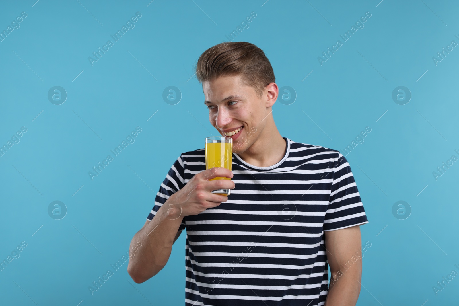 Happy man with glass of orange juice on light blue background. Refreshing drink Photo of Happy man with glass of orange juice on light blue background. Refreshing drink