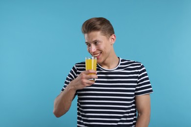 Photo of Happy man with glass of orange juice on light blue background. Refreshing drink