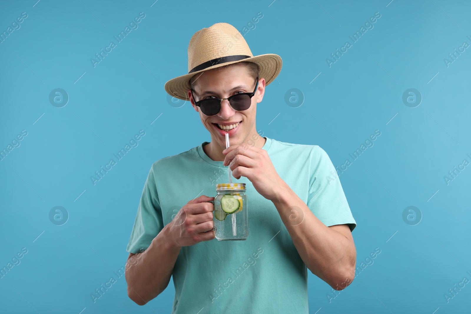 Happy man in sunglasses and hat with mason jar of refreshing drink on light blue background Photo of Happy man in sunglasses and hat with mason jar of refreshing drink on light blue background