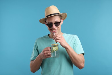 Photo of Happy man in sunglasses and hat with mason jar of refreshing drink on light blue background