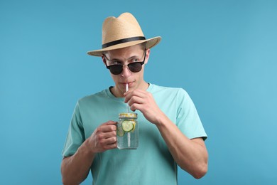 Photo of Man in sunglasses and hat drinking refreshing beverage from mason jar on light blue background