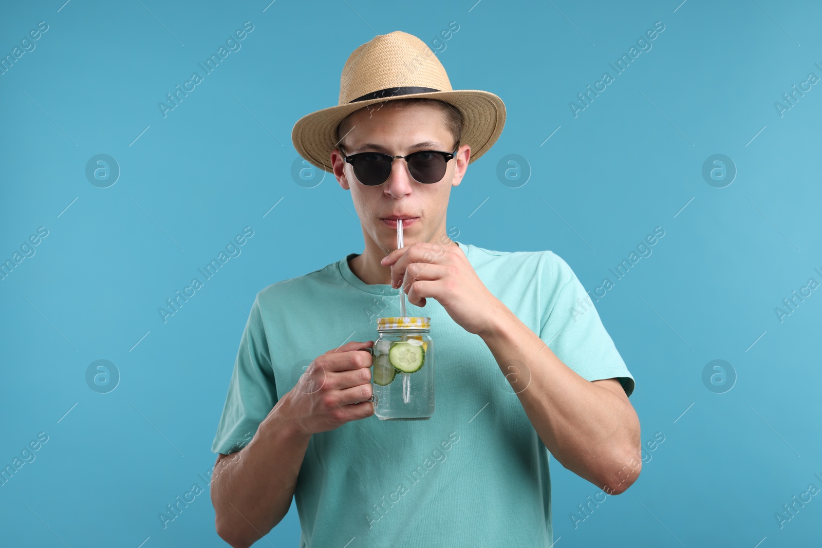 Man in sunglasses and hat drinking refreshing beverage from mason jar on light blue background Photo of Man in sunglasses and hat drinking refreshing beverage from mason jar on light blue background