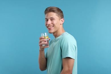 Photo of Happy man with glass of refreshing drink on light blue background