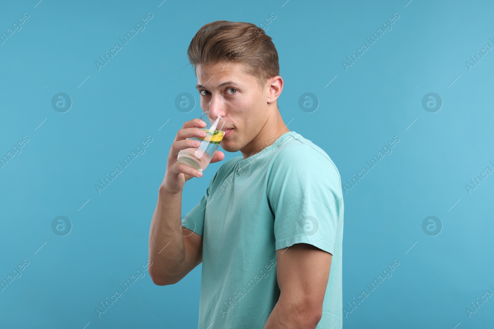 Photo of Man drinking refreshing beverage from glass on light blue background