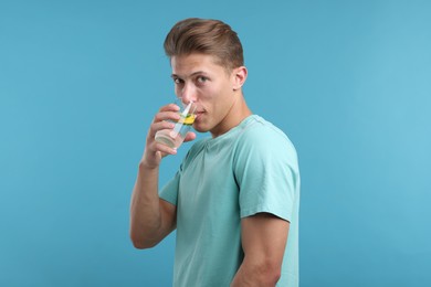 Photo of Man drinking refreshing beverage from glass on light blue background