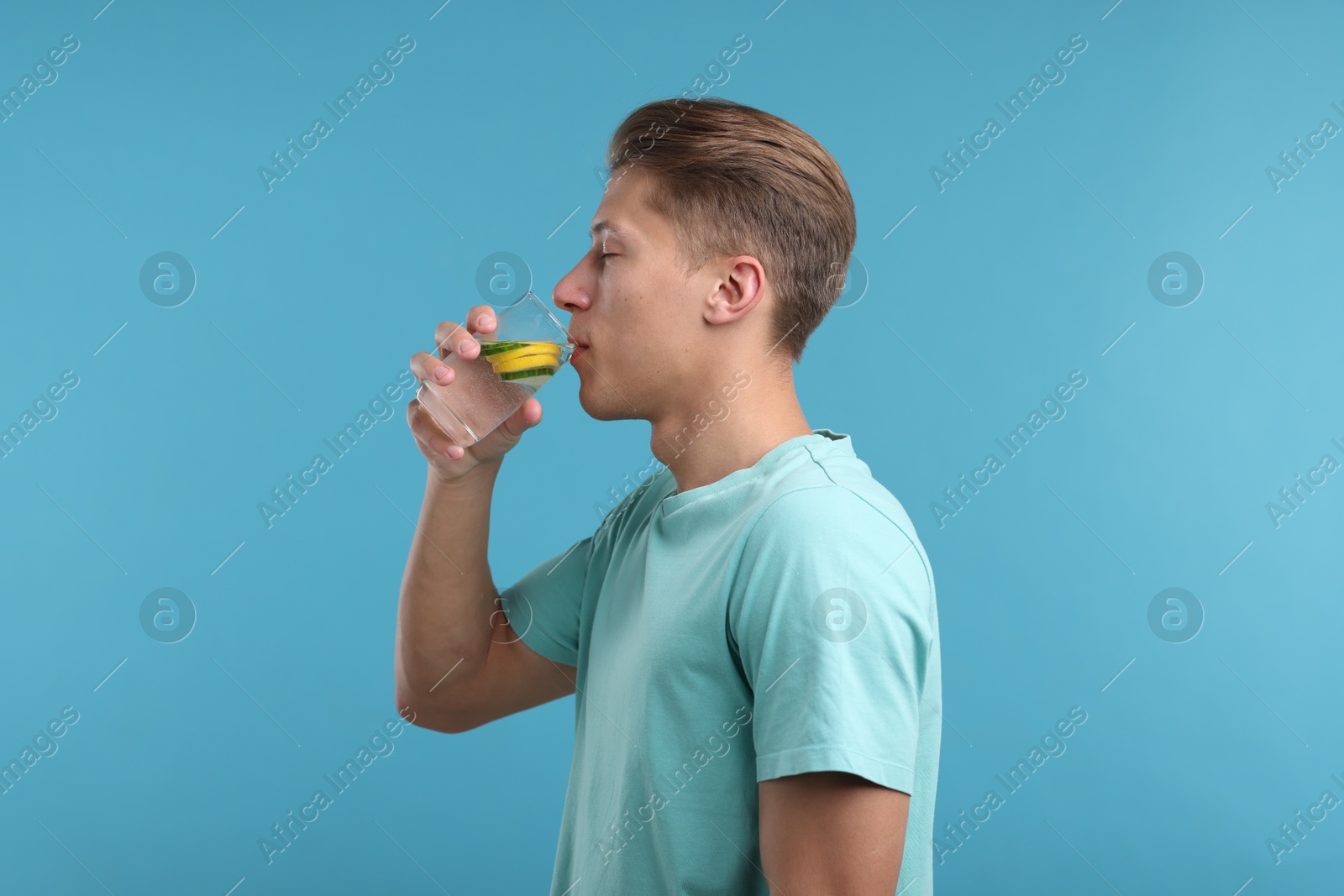 Photo of Man drinking refreshing beverage from glass on light blue background