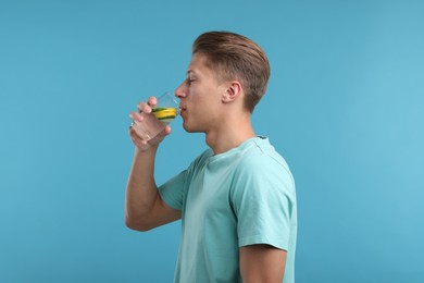 Photo of Man drinking refreshing beverage from glass on light blue background