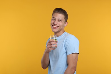 Photo of Happy man with glass of refreshing drink on yellow background
