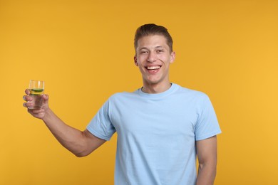 Photo of Happy man with glass of refreshing drink on yellow background