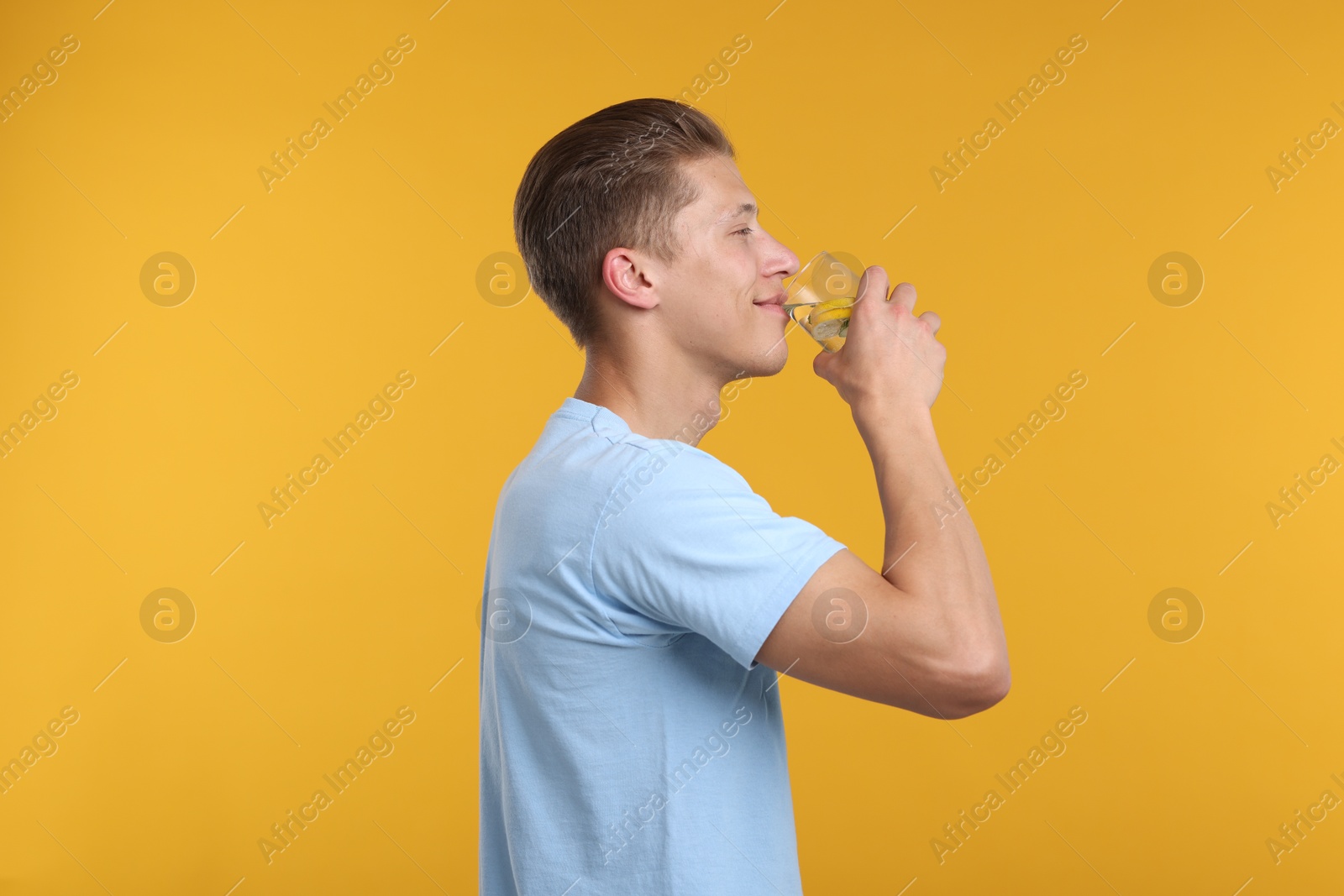 Photo of Man drinking refreshing beverage from glass on yellow background