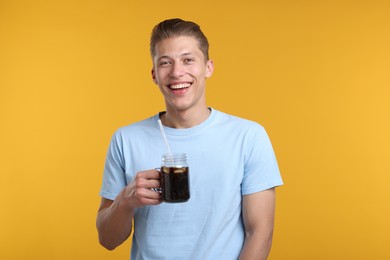 Photo of Happy man with mason jar of refreshing soda drink on yellow background