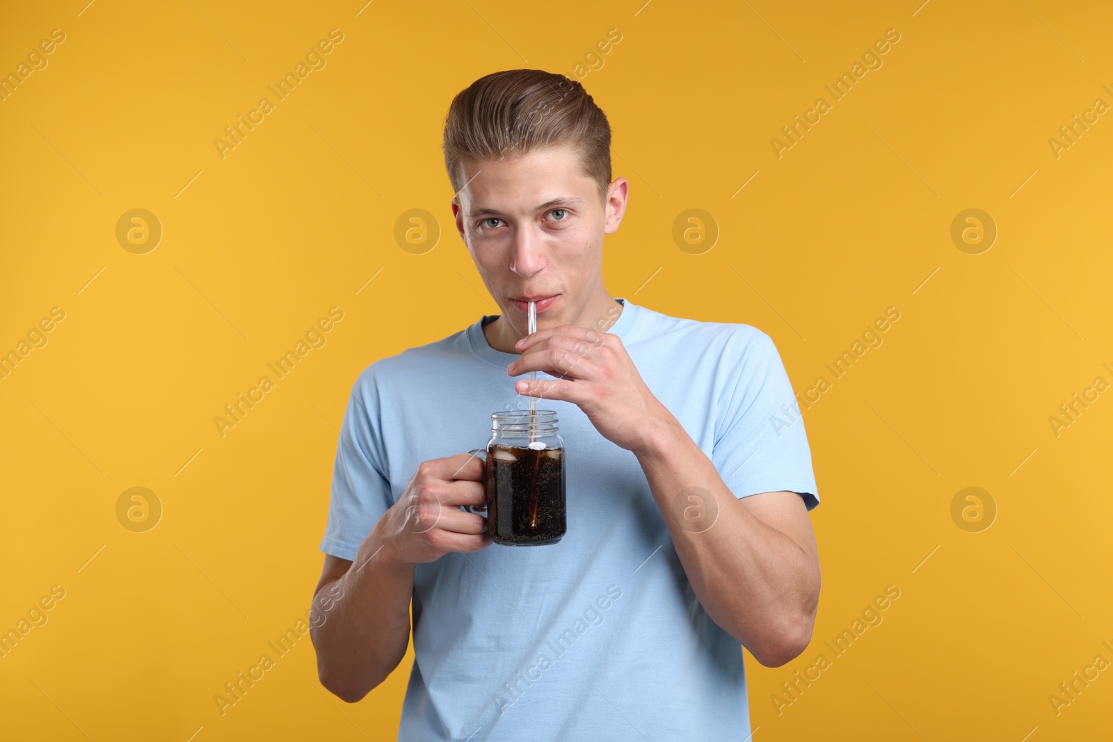 Man drinking refreshing soda drink from mason jar on yellow background Photo of Man drinking refreshing soda drink from mason jar on yellow background