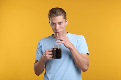 Photo of Man drinking refreshing soda drink from mason jar on yellow background