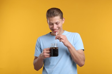 Photo of Happy man with mason jar of refreshing soda drink on yellow background