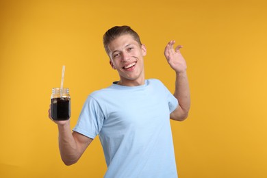 Photo of Happy man with mason jar of refreshing soda drink on yellow background