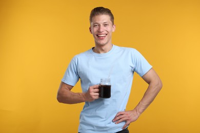 Photo of Happy man with mason jar of refreshing soda drink on yellow background