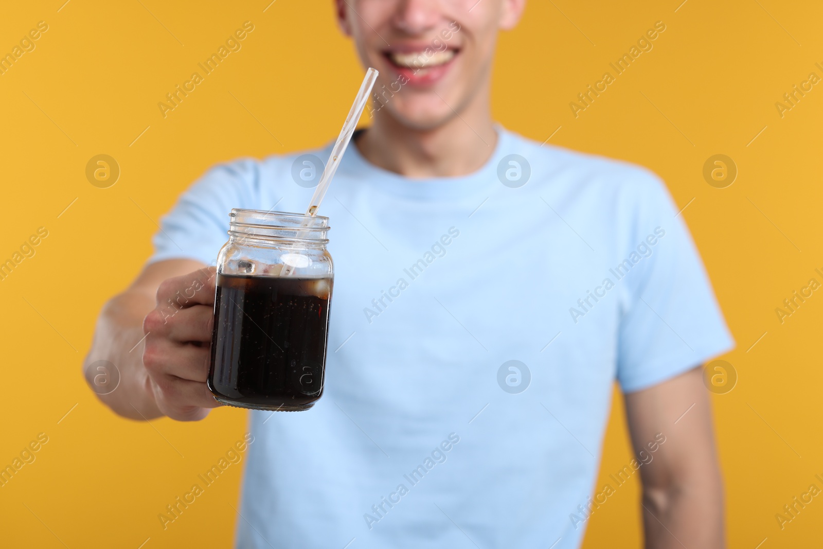 Photo of Happy man with mason jar of refreshing soda drink on yellow background, closeup