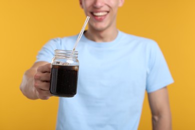 Photo of Happy man with mason jar of refreshing soda drink on yellow background, closeup