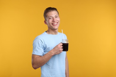 Photo of Happy man with mason jar of refreshing soda drink on yellow background