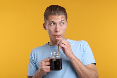 Photo of Man drinking refreshing soda drink from mason jar on yellow background