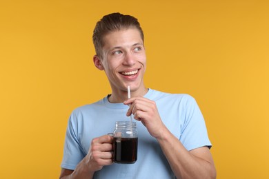 Photo of Happy man with mason jar of refreshing soda drink on yellow background