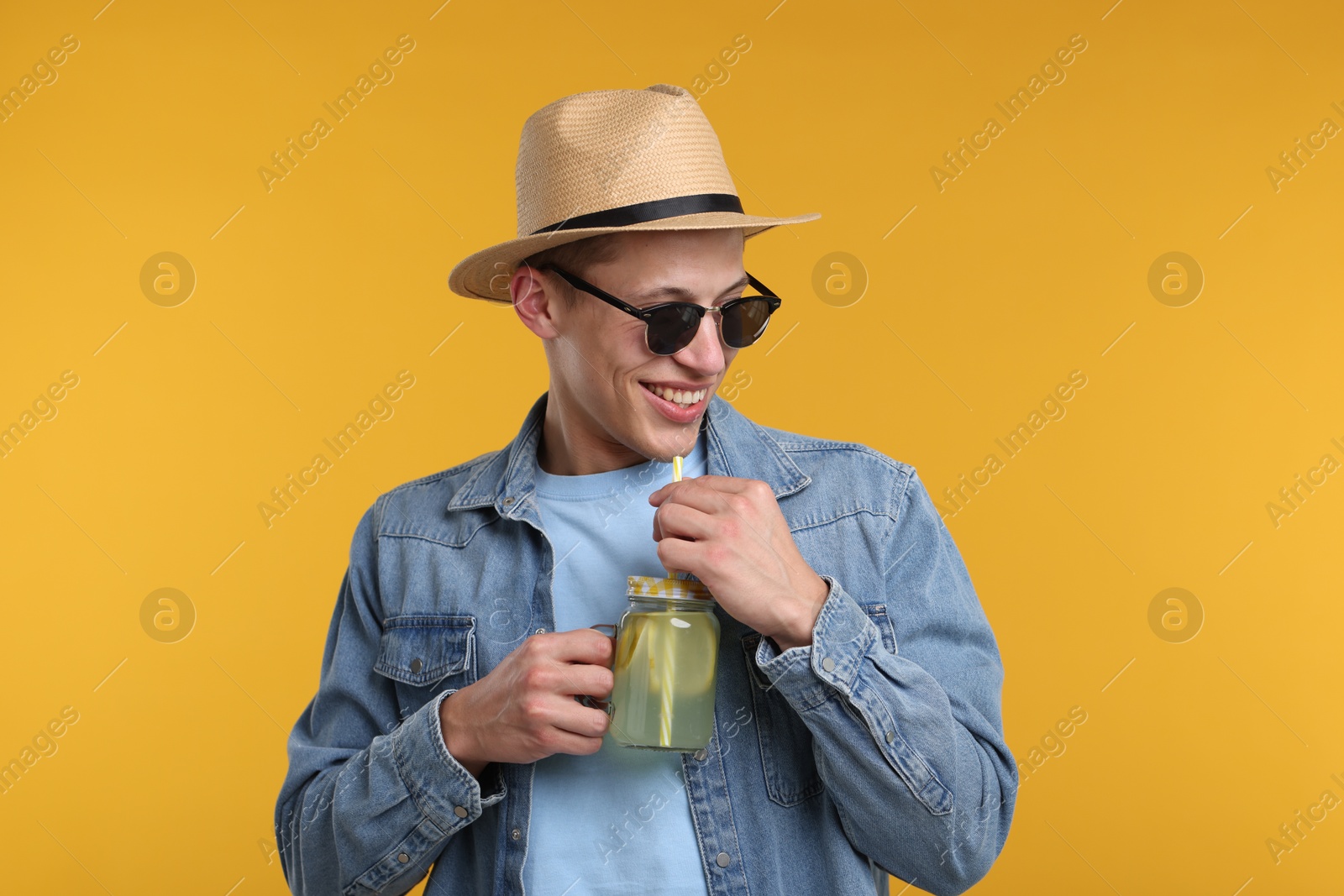 Happy man in hat and sunglasses with mason jar of lemonade on yellow background. Refreshing drink Photo of Happy man in hat and sunglasses with mason jar of lemonade on yellow background. Refreshing drink