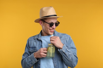 Photo of Happy man in hat and sunglasses with mason jar of lemonade on yellow background. Refreshing drink