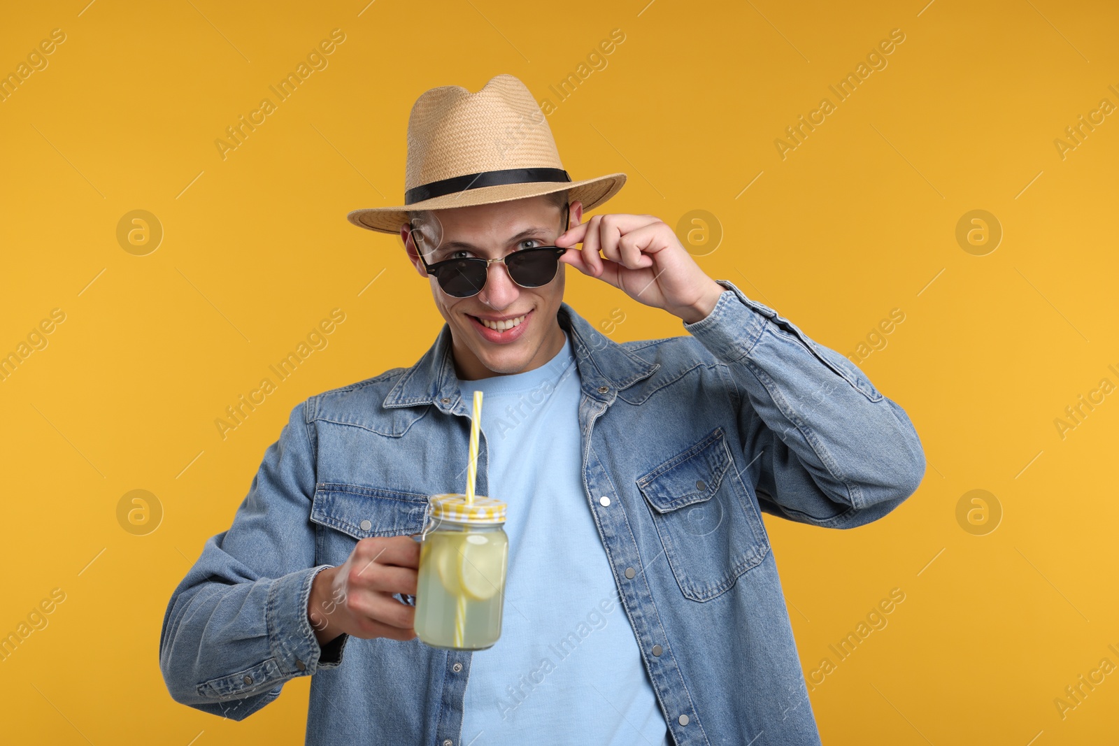 Happy man in hat and sunglasses with mason jar of lemonade on yellow background. Refreshing drink Photo of Happy man in hat and sunglasses with mason jar of lemonade on yellow background. Refreshing drink