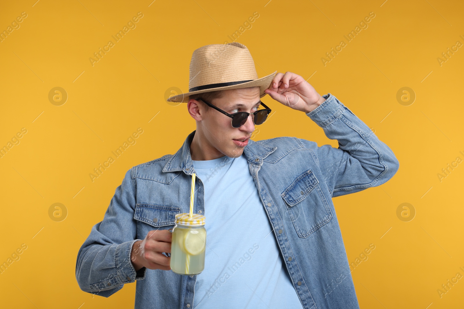 Photo of Man in hat and sunglasses with mason jar of lemonade on yellow background. Refreshing drink