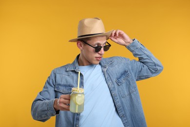Photo of Man in hat and sunglasses with mason jar of lemonade on yellow background. Refreshing drink