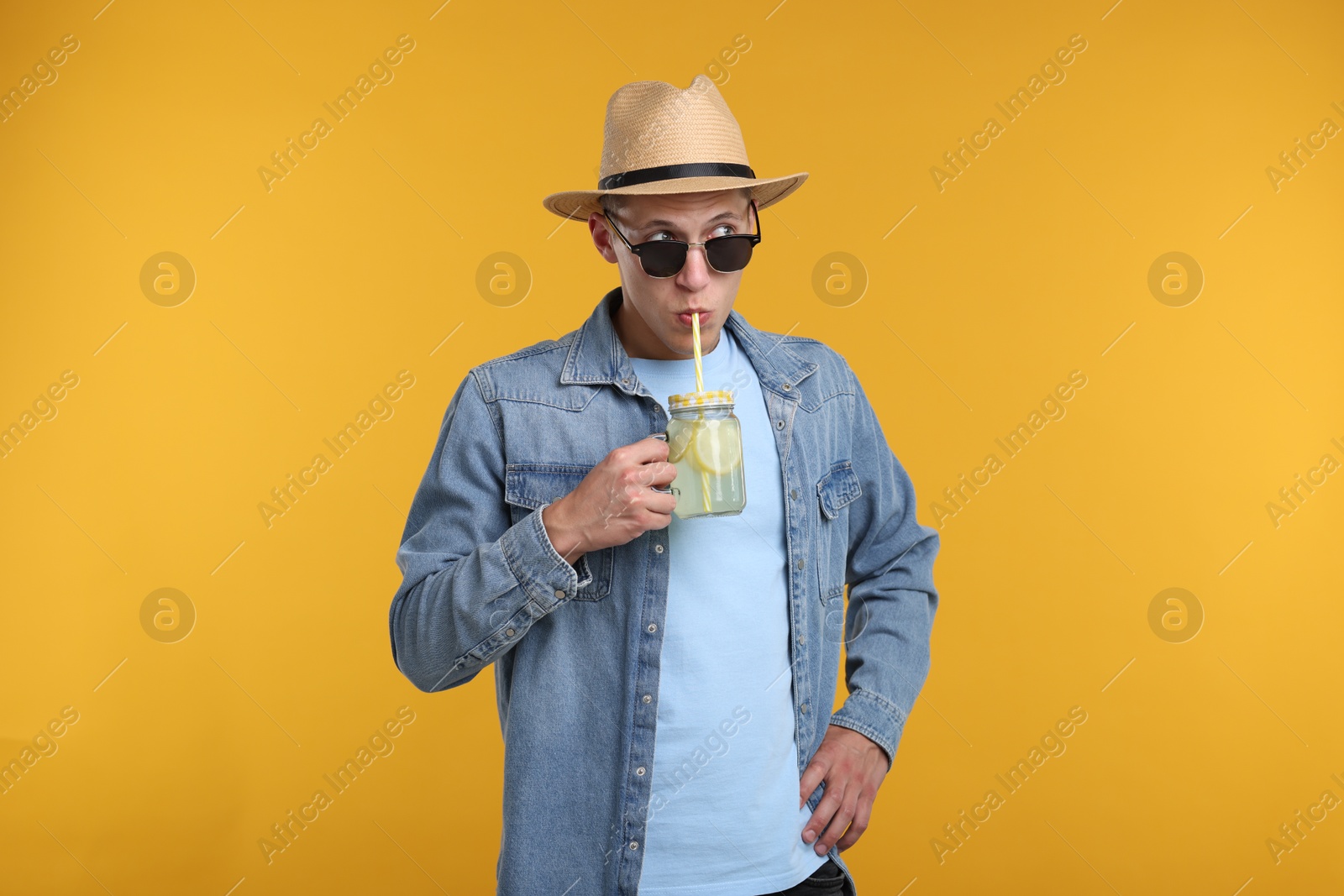 Man in sunglasses and hat drinking lemonade from mason jar on yellow background. Refreshing drink Photo of Man in sunglasses and hat drinking lemonade from mason jar on yellow background. Refreshing drink