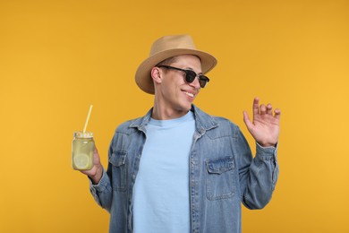 Photo of Happy man in hat and sunglasses with mason jar of lemonade on yellow background. Refreshing drink