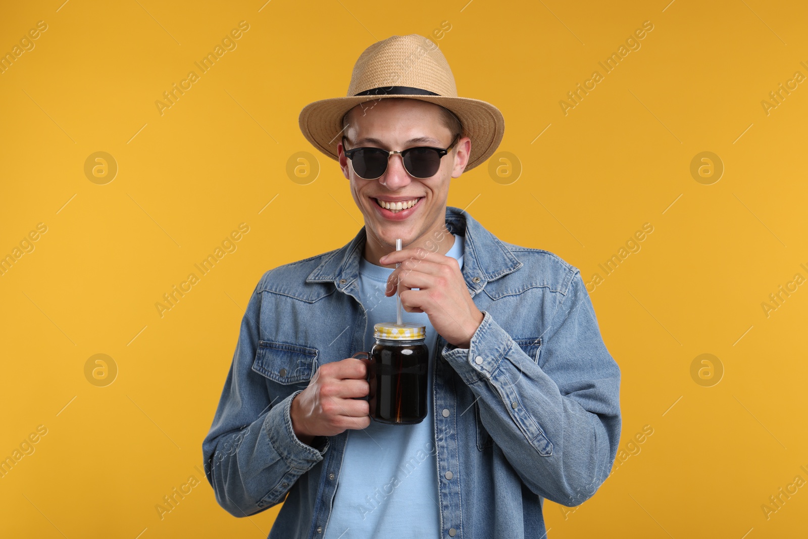 Happy man in sunglasses and hat with mason jar of refreshing soda drink on yellow background Photo of Happy man in sunglasses and hat with mason jar of refreshing soda drink on yellow background