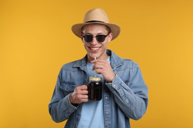 Photo of Happy man in sunglasses and hat with mason jar of refreshing soda drink on yellow background