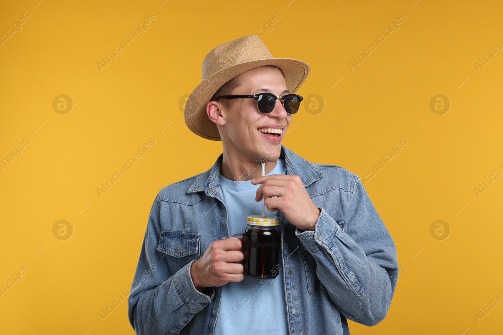 Happy man in sunglasses and hat with mason jar of refreshing soda drink on yellow background Photo of Happy man in sunglasses and hat with mason jar of refreshing soda drink on yellow background