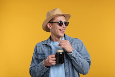 Photo of Happy man in sunglasses and hat with mason jar of refreshing soda drink on yellow background