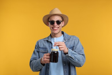 Photo of Happy man in sunglasses and hat with mason jar of refreshing soda drink on yellow background