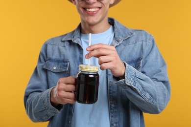 Photo of Happy man with mason jar of refreshing soda drink on yellow background, closeup