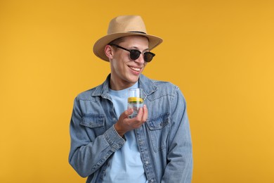 Photo of Happy man in sunglasses and hat with glass of refreshing drink on yellow background