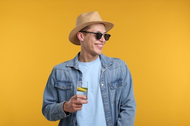 Photo of Happy man in sunglasses and hat with glass of refreshing drink on yellow background